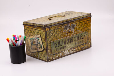 Ancienne boite en métal avec des peintures de panier en osier qui paradoxalement donne impression de coffre-fort avec des teintes dorées-brunes de la marque belge de chocolat Senez-Sturbelle