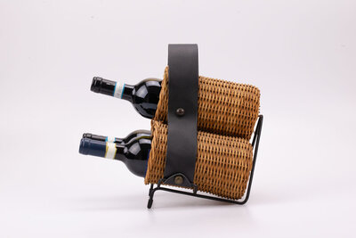Porte-bouteilles artisanal en osier avec une lanière en simili-cuir et une ossature en métal pour tenir l'objet légèrement penché.