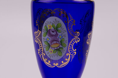 Vase en cristal bleu dans un style bohème avec des motifs de fleurs et plusieurs liserés dorés qui structurent l'objet