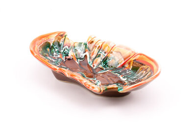 Un grand plat en céramique signé "Vallauris". Il est dans les tons orangés et brun réhaussé par des mélanges de vert et de blanc.