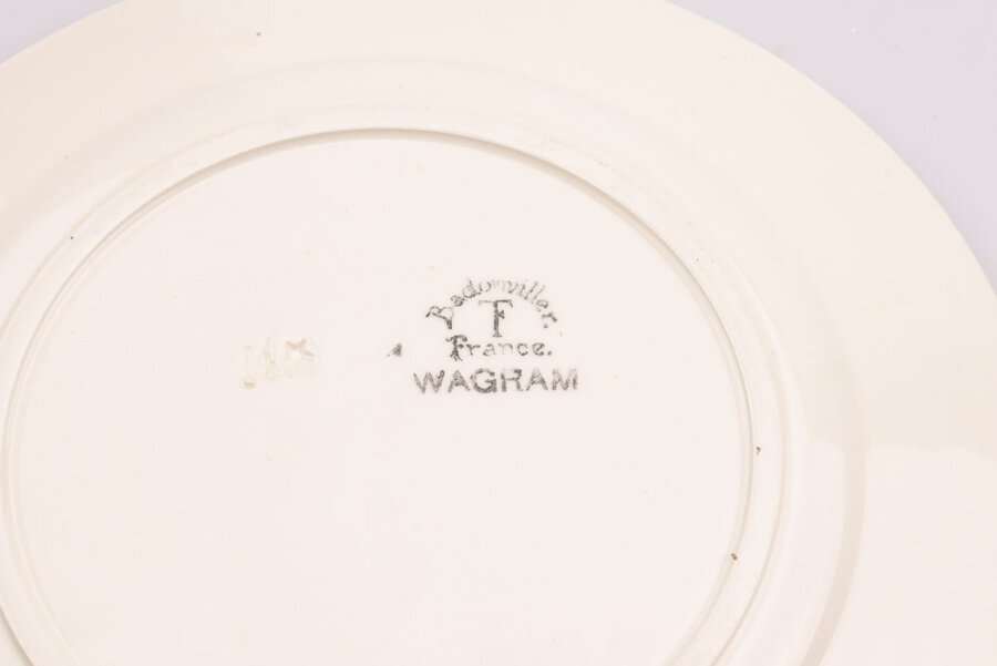 Signature sur assiette plate vintage en céramique blanche avec des motifs bleus et fabriqué par Wagram de Badonviller