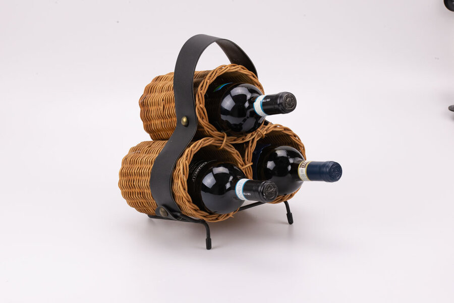 Porte-bouteilles artisanal en osier avec une lanière en simili-cuir et une ossature en métal pour tenir l'objet légèrement penché.