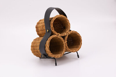 Porte-bouteilles artisanal en osier avec une lanière en simili-cuir et une ossature en métal pour tenir l'objet légèrement penché.