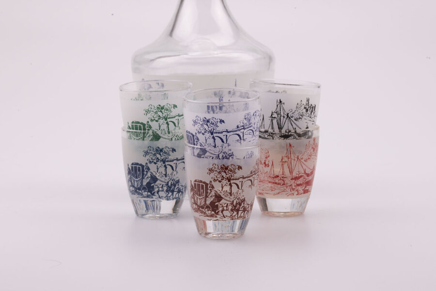 Service à liqueur en cristal d'Arques avec 1 bouteille et 6 petits verres dans leur boite d'origine. Sur chacun des objets, il y a des dessins bleus, rouges, verts ou bruns représentant un paysage